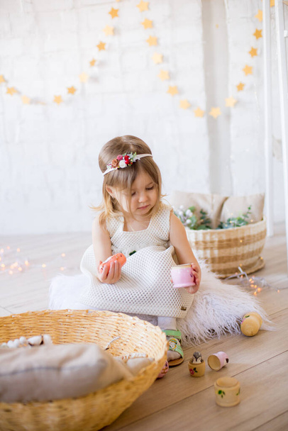 Little cute girl in a white dress plays in a bright children's room, decorated with toys and garlands. - Foto, imagen