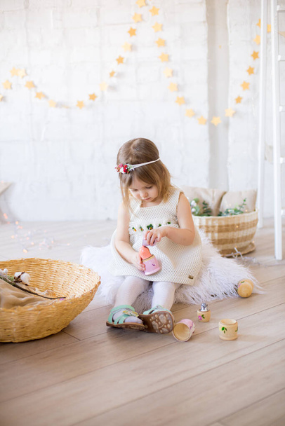Little cute girl in a white dress plays in a bright children's room, decorated with toys and garlands. - Fotoğraf, Görsel