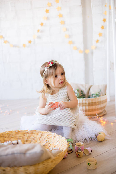 Petite fille mignonne dans une robe blanche joue dans une chambre d'enfant lumineuse, décorée avec des jouets et des guirlandes
. - Photo, image