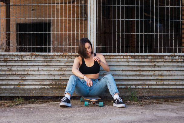 Young woman sitting on her skate in an old industrial street - Photo, Image
