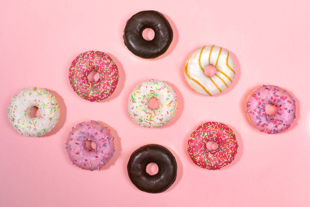 Doughnuts with multicolored glaze laid out in form of rhombus on trendy pink background. Doughnuts are traditional sweet pastries. Creative layout, top view, flat lay. - Foto, Bild