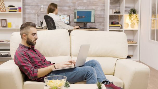 Όμορφος ελεύθερος επαγγελματίας που εργάζεται σε φορητό υπολογιστή, ενώ κάθεται στον καναπέ - Φωτογραφία, εικόνα