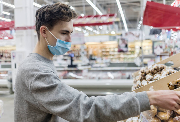 Young man wearing disposable medical mask shopping in supermarket during coronavirus pneumonia outbreak. Protection et prévention en période d'épidémie. Covid-19 - Photo, image