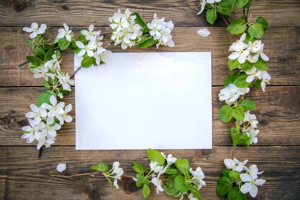 A branch of a blooming apple tree with white flowers and a sheet of paper on a rustic wooden background, with a copy space, top view - Foto, Bild