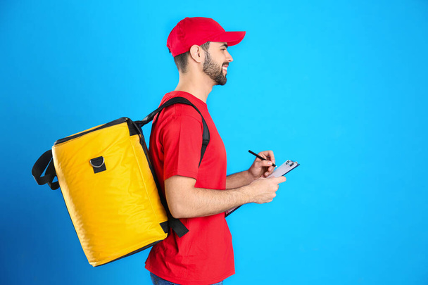 Courier with thermo bag and clipboard on light blue background, space for text. Food delivery service - Foto, immagini