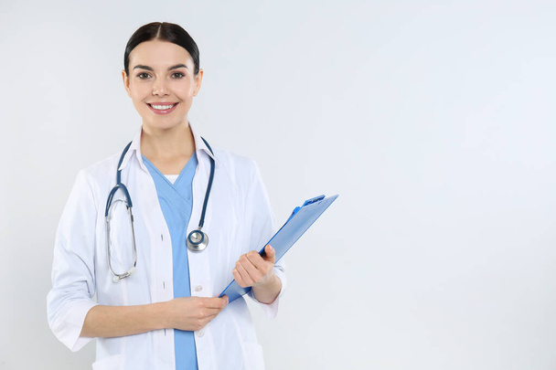 Portrait of young doctor with stethoscope and clipboard on white background - Foto, Imagem