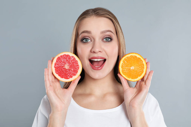 Emotional young woman with cut orange and grapefruit on grey background. Vitamin rich food - Valokuva, kuva
