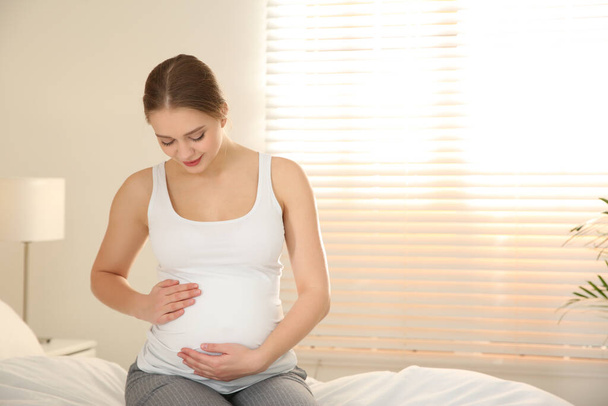 Young pregnant woman on bed at home. Space for text - Photo, Image