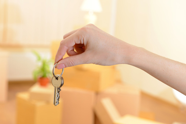 Female hand with keys ob stack of cartons background: moving house concept - Photo, Image