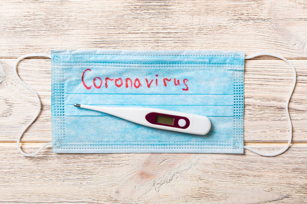 Stapel von medizinischen Schutzmasken mit Coronavirus-Wort und einem Thermometer auf hölzernem Hintergrund. Atemwegssyndrom. Schützen Sie Ihr Gesundheitskonzept. - Foto, Bild