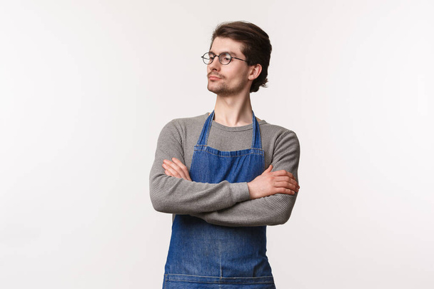 Tailliertes Porträt eines ernst dreinblickenden, entschlossenen männlichen Restaurantmanagers, der Mitarbeiter ansieht, die Arbeit kontrolliert, die Hände über der Brust verschränkt wie ein Profi, der wegstarrt, weißer Hintergrund - Foto, Bild