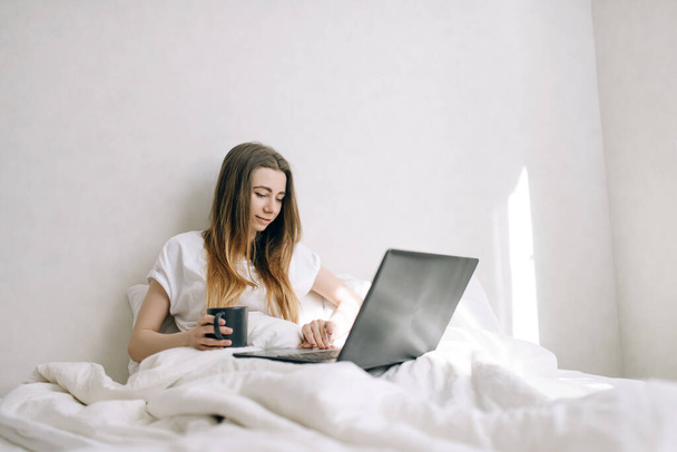 Nuori nainen käyttää sylimikroa sängyssään. Kotona työskentely
 - Valokuva, kuva