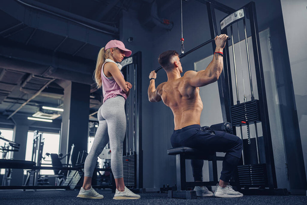 young male bodybuilder doing heavy weight exercise while his girlfriend watching him - Valokuva, kuva