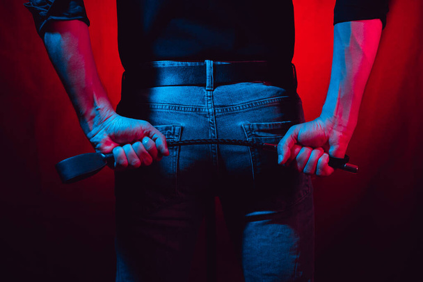 um homem sexy detém um bdsm chicote em um fundo vermelho atrás de suas costas - Foto, Imagem