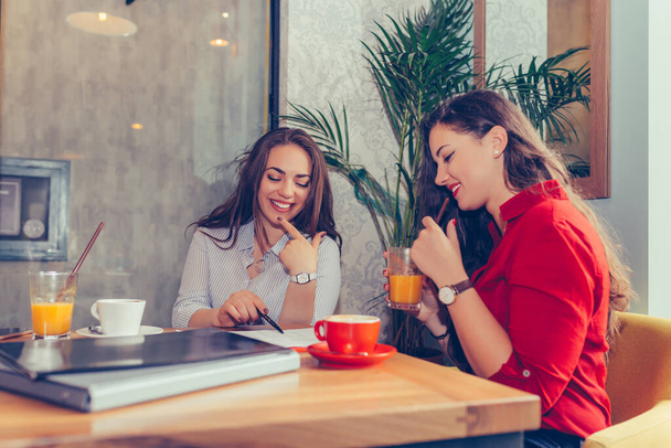 Χαρούμενες γυναίκες φίλοι, μαθητές που διαβάζουν σημειώσεις μαζί, δείχνοντας που να υπογράψουν ένα συμβόλαιο, να μιλούν και να πίνουν καφέ ενώ κάθονται στο τραπέζι στο καφέ. -Εικόνα - Φωτογραφία, εικόνα