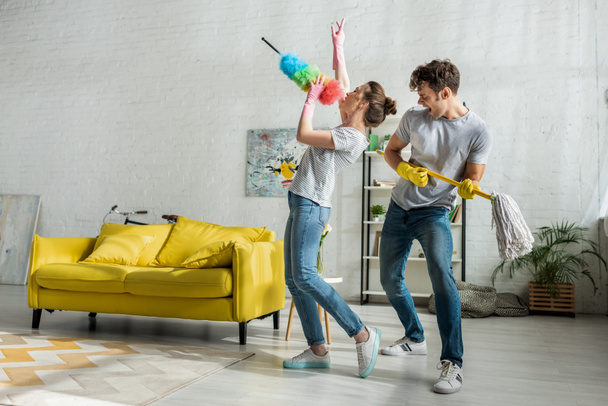 mężczyzna i kobieta ze śpiewem gospodarstwa domowego podczas wiosennego sprzątania w salonie  - Zdjęcie, obraz