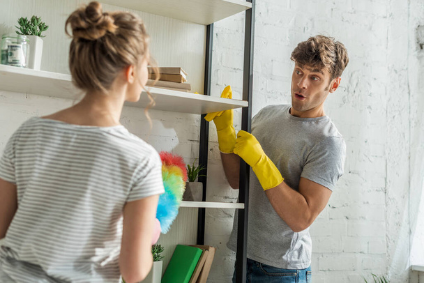 selective focus of surprised man cleaning rack shelves near girl at home  - Photo, Image