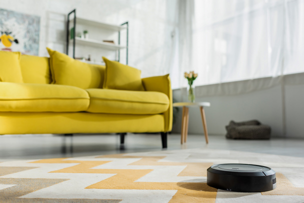 selective focus of robotic vacuum cleaner washing carpet near sofa in living room  - Valokuva, kuva