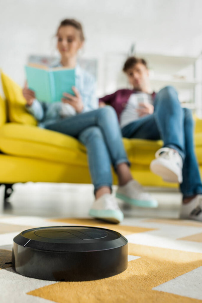 selective focus of robotic vacuum cleaner washing carpet near man and woman in living room  - Photo, Image
