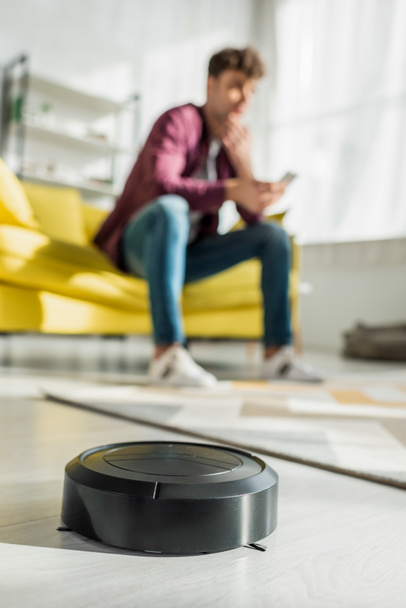 selective focus of robotic vacuum cleaner washing carpet near man in living room - Photo, Image