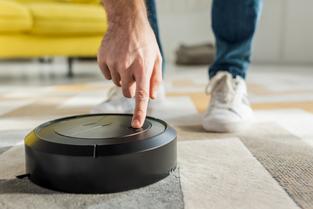cropped view of man pointing with finger at robotic vacuum cleaner in living room - Zdjęcie, obraz