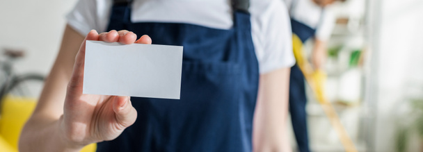 panoramic shot of cleaner in uniform holding blank card  - Foto, afbeelding