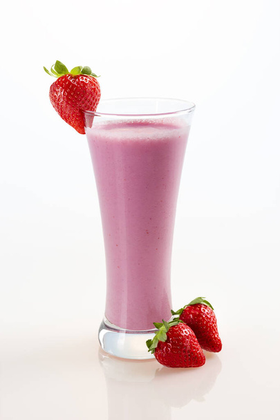 Glass of delicious milkshake with fresh strawberries placed against white background - Фото, изображение
