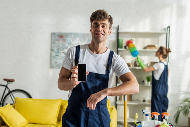 selective focus of happy and handsome cleaner holding smartphone with blank screen  - Foto, Imagen