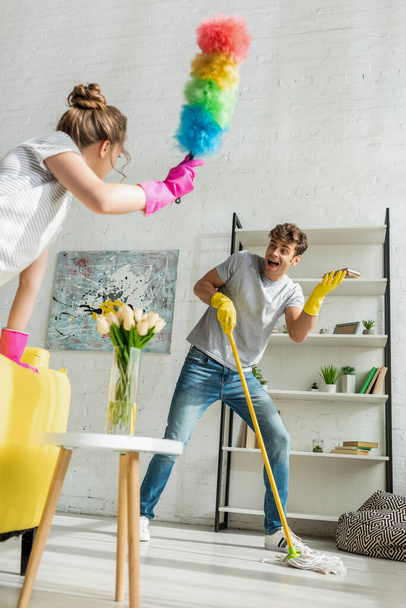 selective focus of handsome man looking at young woman doing spring cleaning in apartment  - Photo, Image