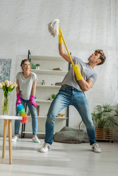 young and surprised woman looking at handsome man with mop  - Foto, Bild