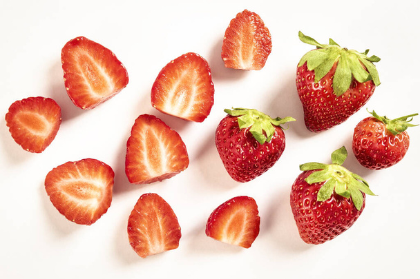 Vue de dessus de fraises entières et tranchées fraîches et juteuses sur une table blanche. Délicieux fruit bio de première classe comme concept de vitamines estivales. Aliments sucrés sains, vitamines et concept fruité
. - Photo, image