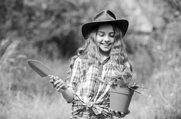 Planting plants. Happy childhood. Child in hat with shoulder blade small shovel hoe. Happy smiling gardener girl. Ranch girl. Little kid hold flower pot. Spring country works. Happy childrens day - Fotografie, Obrázek