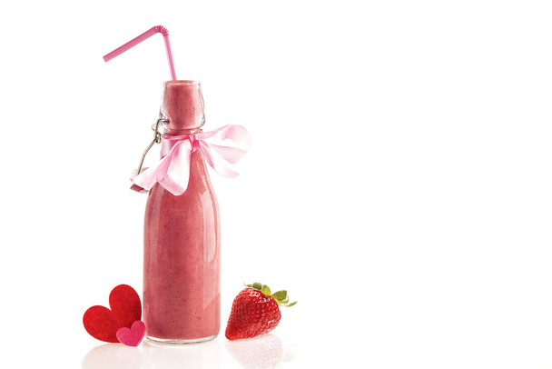 Delicious and nutritious smoothie made from fresh strawberries in a glass bottle with a straw, a pink bow and cloth hearts. Gift to give and share the lovers on Valentine's day. White background. - Foto, Imagen
