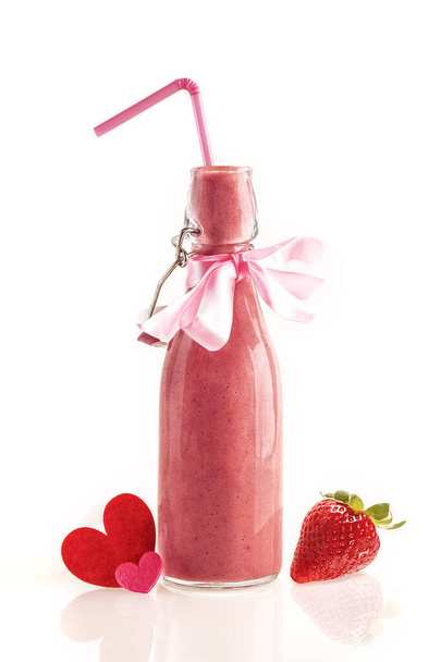 Delicious and nutritious smoothie made from fresh strawberries in a glass bottle with a straw, a pink bow and cloth hearts. Gift to give and share the lovers on Valentine's day. White background. - Фото, зображення
