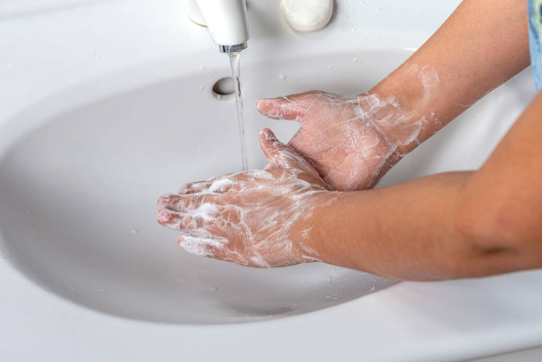 Frau wäscht Hand mit Seifenschaum und Leitungswasser im Badezimmer. Händewaschen unter dem Wasserhahn am Waschbecken zur persönlichen Hygiene, um Grippe vorzubeugen. - Foto, Bild