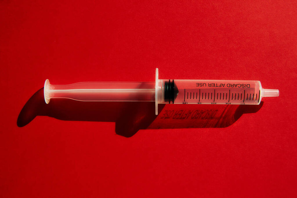 Одноразовый медицинский шприц без инъекционной иглы на красном фоне с бликами и тенями. Концепция коронавируса. Остановить коронавирус 2019 года (2019-nCoV)
) - Фото, изображение