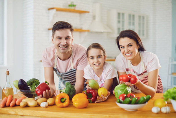 Happy family smiling at a table with fresh vegetables make salad in the kitchen. - Foto, Imagem