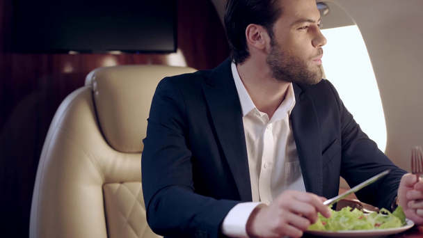 飛行機で旅をしながら新鮮なサラダを食べるハンサムなビジネスマン - 映像、動画