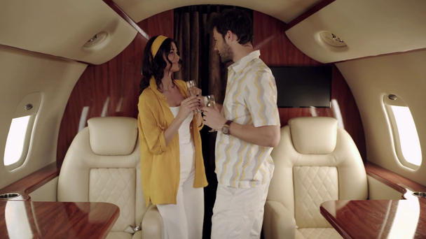 ευτυχισμένο ζευγάρι που κρατάει ποτήρια σαμπάνιας και χορεύει ενώ ταξιδεύει με αεροπλάνο - Πλάνα, βίντεο