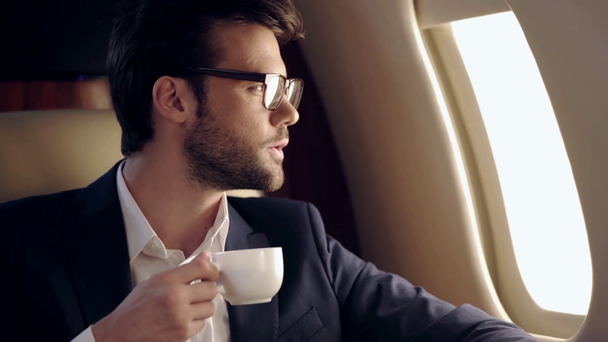 przystojny biznesmen pijący kawę podczas podróży samolotem - Materiał filmowy, wideo