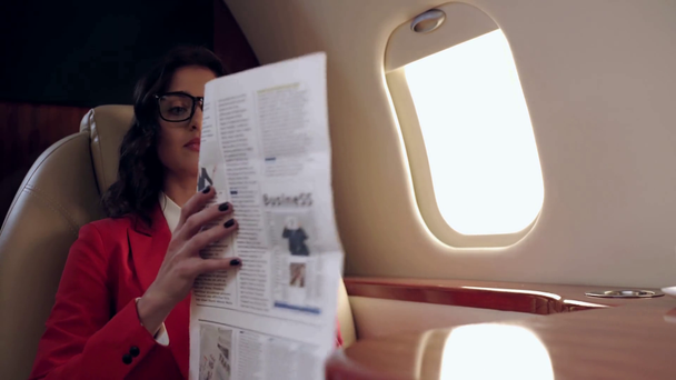 attentive businesswoman reading business newspaper while traveling by plane - Кадры, видео