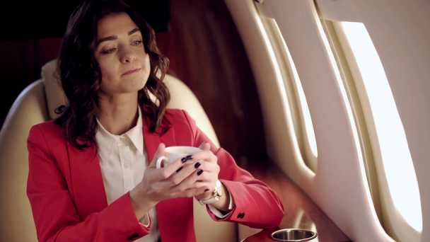 kaunis liikenainen juo kahvia matkustaessaan lentokoneella
 - Materiaali, video