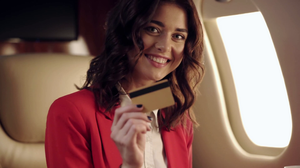 Genç iş kadını kameraya gülümsüyor ve uçakta kredi kartını gösteriyor. - Video, Çekim