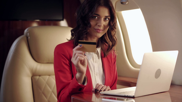 businesswoman using laptop and showing credit card while traveling by plane - Imágenes, Vídeo