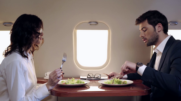 νέοι επιχειρηματίες που μιλούν και τρώνε σαλάτα ενώ ταξιδεύουν με αεροπλάνο - Πλάνα, βίντεο