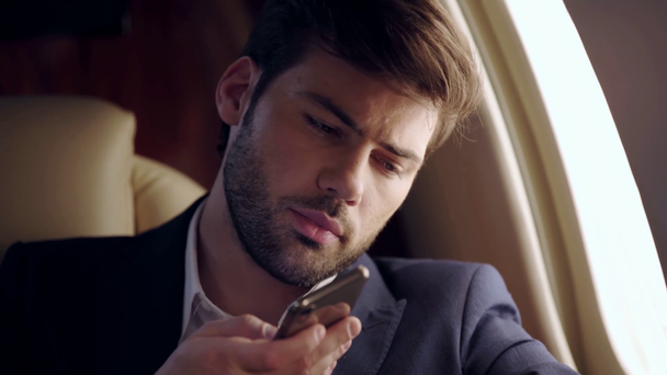 серйозний бізнесмен розмовляє по смартфону під час подорожі літаком
 - Кадри, відео
