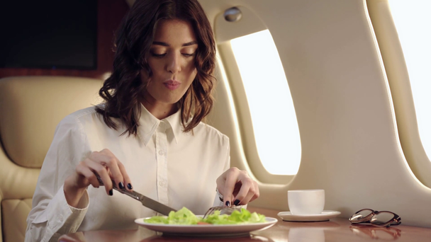 Lächelnde Geschäftsfrau isst während einer Flugreise frischen Salat - Filmmaterial, Video