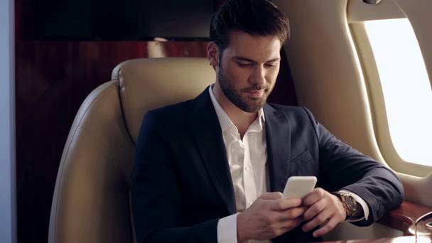 guapo hombre de negocios charlando en el teléfono inteligente mientras viaja en avión
 - Metraje, vídeo