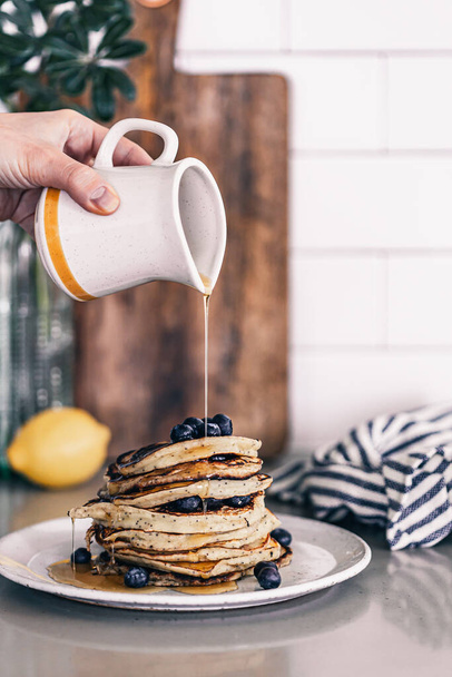 Lemon poppy seed pancakes on grey plate. Fresh blueberries on top. Maple syrup drizzle. Stack of warm pancakes. Breakfast brunch time. Kitchen countertop. Lifestyle food photography. Fluffy pancakes. - Foto, afbeelding