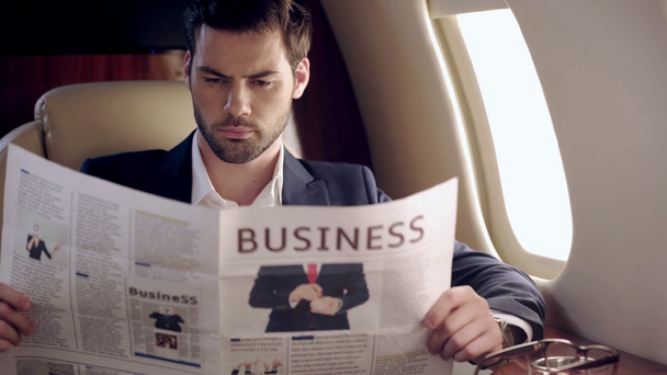 vakava, tarkkaavainen liikemies lukee sanomalehteä matkustaessaan lentokoneella
 - Materiaali, video